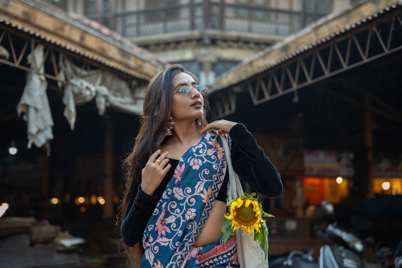 An elegant Indian woman models a traditional saree at a bustling outdoor market in Pune.